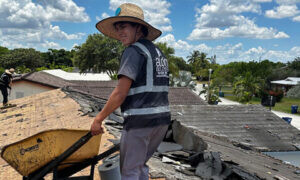 A worker in a hat and Alom Builders attire repairing a roof for a Miami roofing company.