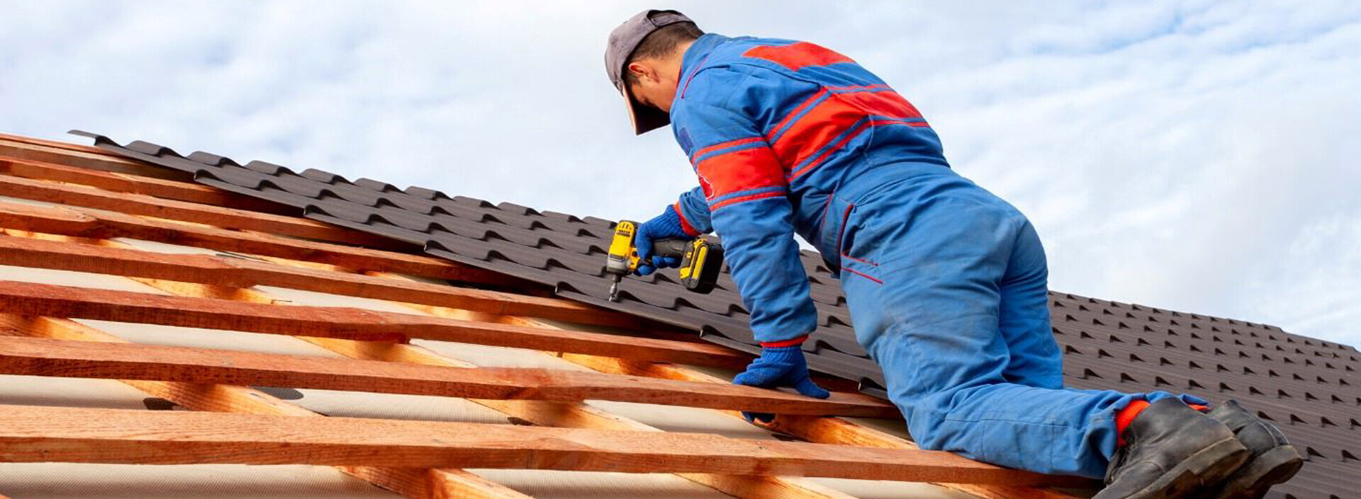 A skilled worker in blue overalls is seen repairing a roof, representing the quality services of Alom Builders Roofing Company.